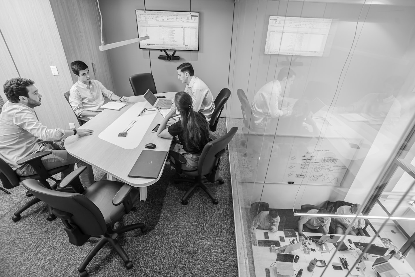 Professionals collaborate around a conference table with laptops and a spreadsheet.