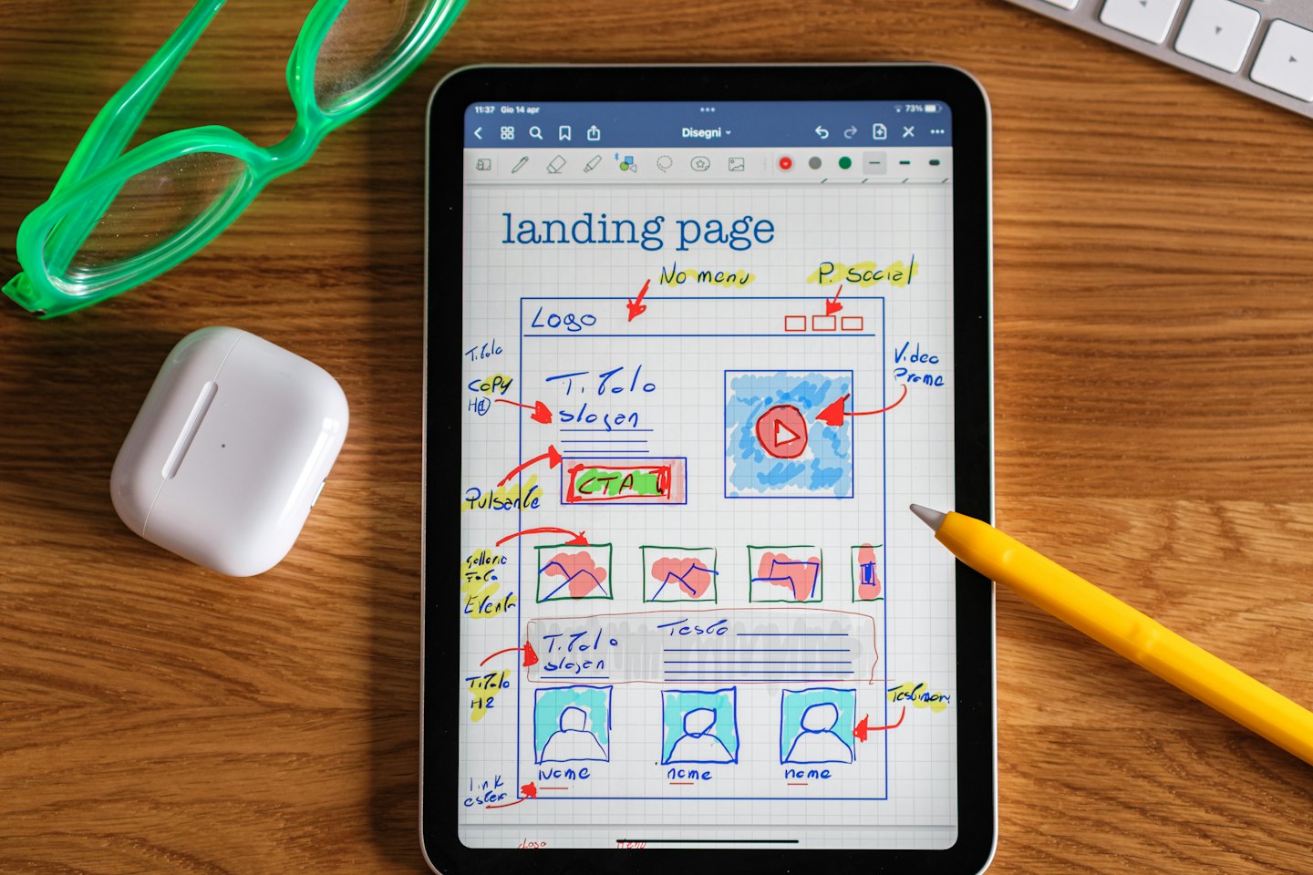 Tablet with wireframe designs lies on a desk with accessories.